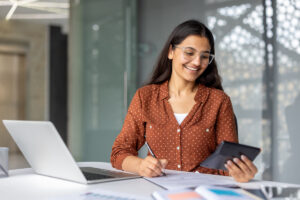Une étudiante souriante utilise une calculatrice pour déclarer vos revenus 2026 sur son ordinateur.