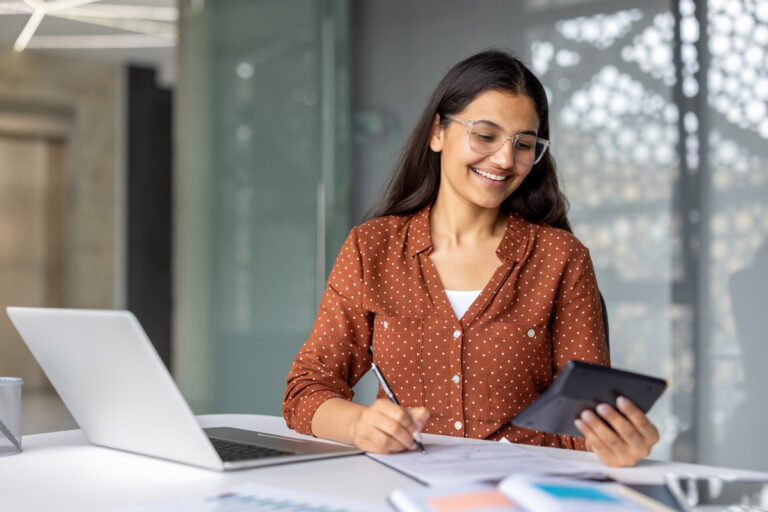 Une étudiante souriante utilise une calculatrice pour déclarer vos revenus 2026 sur son ordinateur.