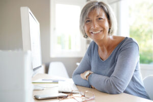 Femme senior souriante travaillant sur ordinateur dans le cadre d'un cumul emploi-retraite en 2026.