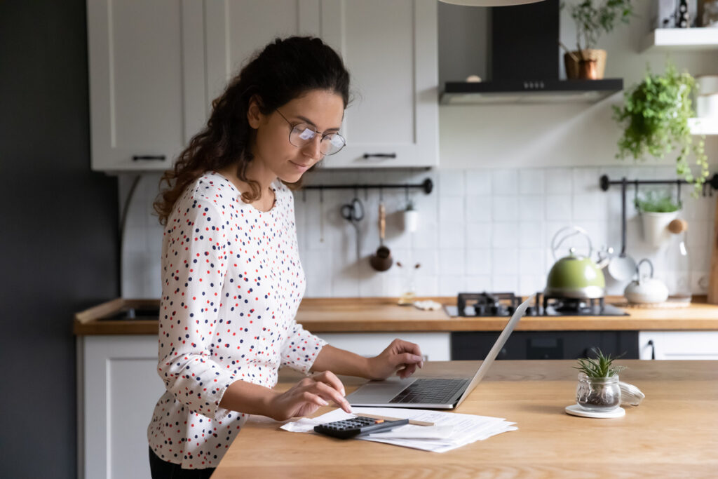 Femme vérifiant son foyer fiscal et ses ressources annuelles imposables sur ordinateur dans sa cuisine.