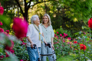 Une femme senior souriante dans un jardin fleuri avec une jeune femme, illustrant le bénéfice d'un départ en retraite anticipée pour carrière longue.