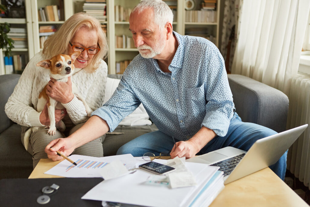 Un couple senior examine des documents administratifs et un graphique devant un ordinateur portable pour calculer leurs trimestres de retraite.