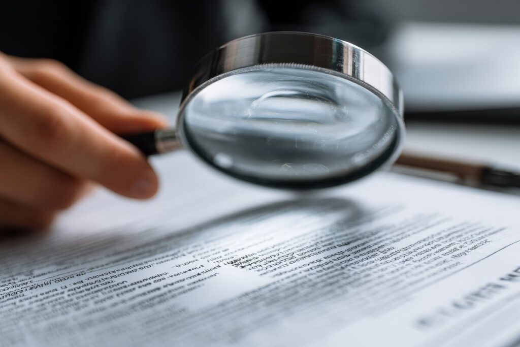 Gros plan sur une main tenant une loupe au-dessus d'un document administratif pour traquer les anomalies d'un relevé de carrière Info-Retraite.