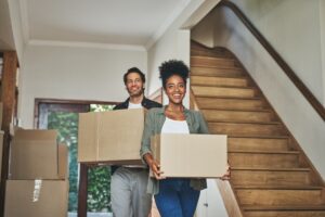 Deux jeunes colocataires souriants portant des cartons de déménagement dans un nouvel appartement.