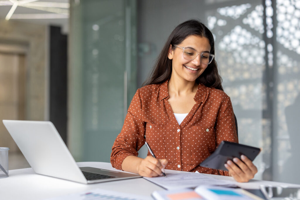 Une jeune femme devant son ordinateur utilisant une calculatrice pour simuler son budget logement.