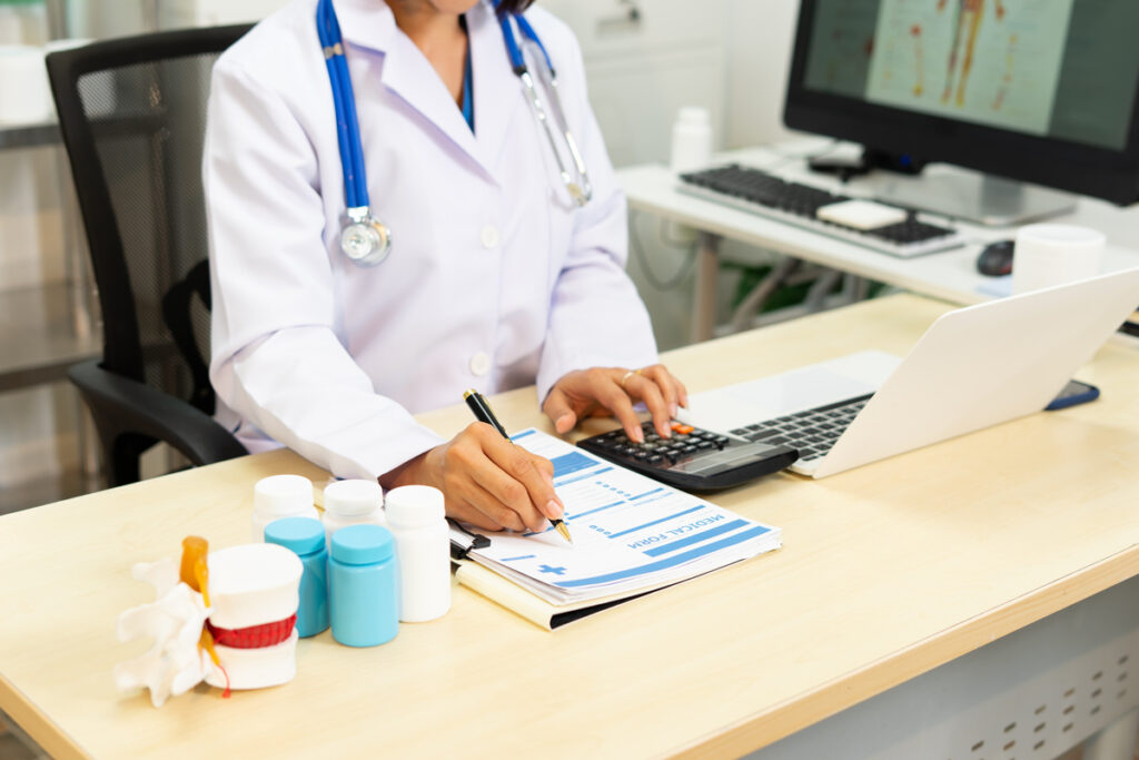 Un médecin utilise une calculatrice au-dessus d'un formulaire médical pour vérifier l'éligibilité selon le barème des plafonds CSS 2026.