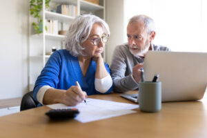 Un couple de seniors à la maison calcule ses ressources sur ordinateur après une fin de droits ARE pour demander l'ASS.