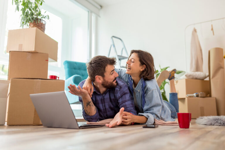 Un couple heureux en plein emménagement utilisant un ordinateur pour déclarer le fait de vivre en concubinage sur le site de la CAF.