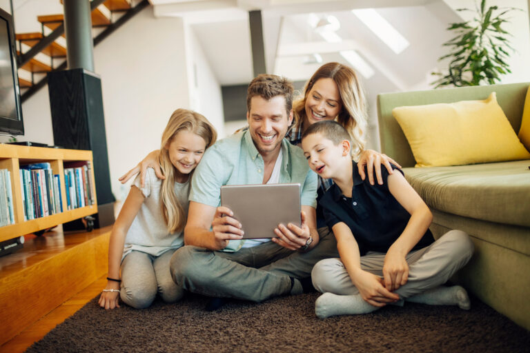 Une famille unie utilise une tablette dans son salon pour vérifier les droits et le calcul du quotient familial sur l'application de la CAF.