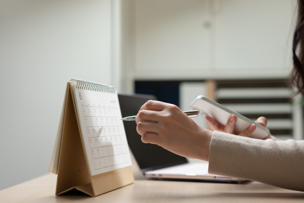 Une gestionnaire pointe un stylo vers un calendrier de bureau pour planifier les échéances obligatoires de son compte bailleur CAF.