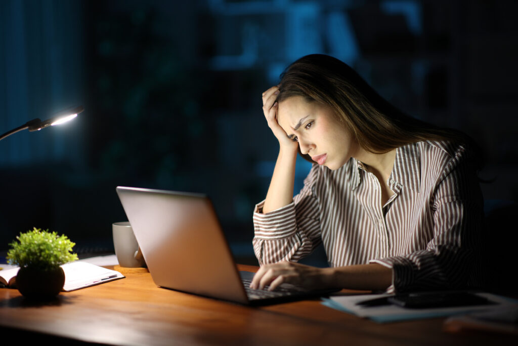 Une femme stressée se prend la tête entre les mains face à son ordinateur portable suite à un problème de dossier CAF en ligne.