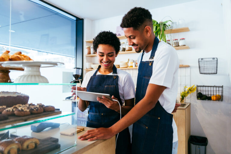 Deux salariés souriants dans un commerce utilisant une tablette, concernés par la prime d'activité et temps partiel.