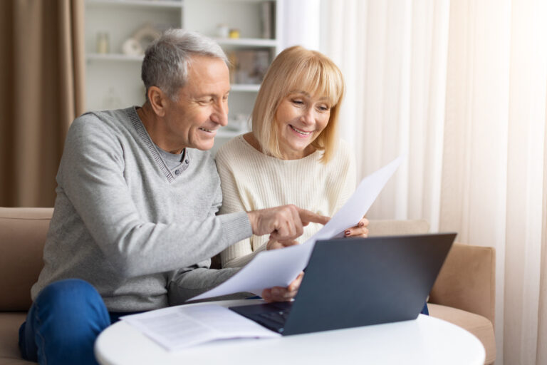 Couple de retraités consultant un ordinateur et des documents pour leurs démarches de retraite et aides