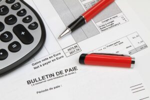 Bulletin de paie avec une calculatrice, illustrant la prise en compte de la prime Macron pour le calcul des aides de la CAF.