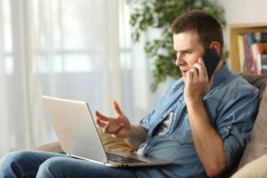Homme préoccupé au téléphone et sur son ordinateur face aux délais de traitement CAF et aux blocages de son dossier.