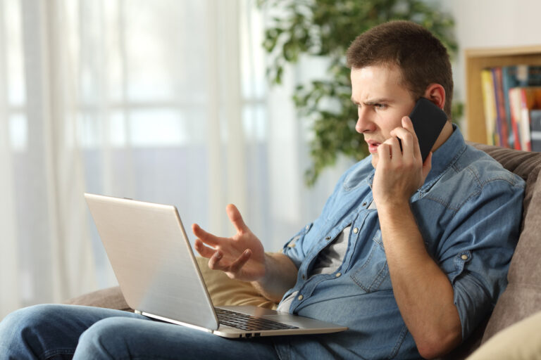 Homme préoccupé au téléphone et sur son ordinateur face aux délais de traitement CAF et aux blocages de son dossier.